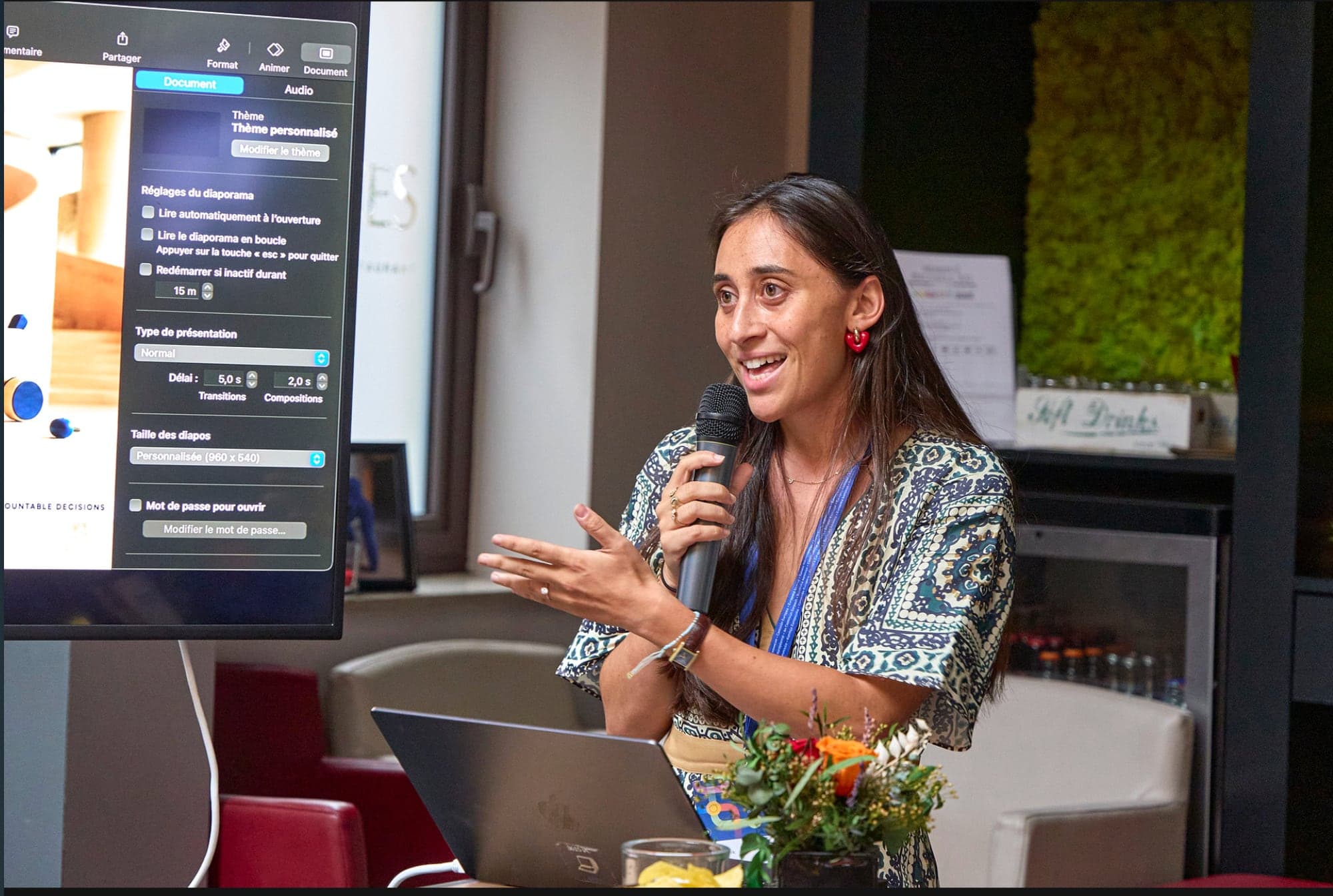 Naomie Halioua giving the keynote, microphone in hand, slides on the screen behind her