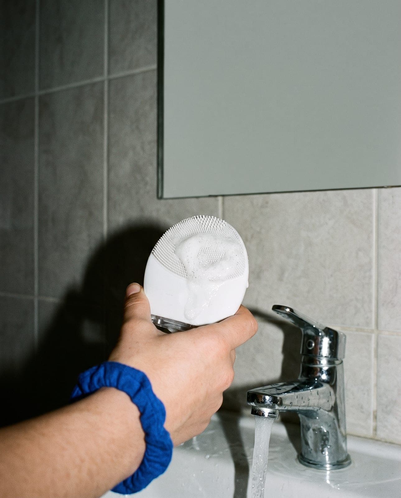 Brosse nettoyante en silicone blanche sous le robinet, mousse sur les poils, un chouchou bleu au poignet