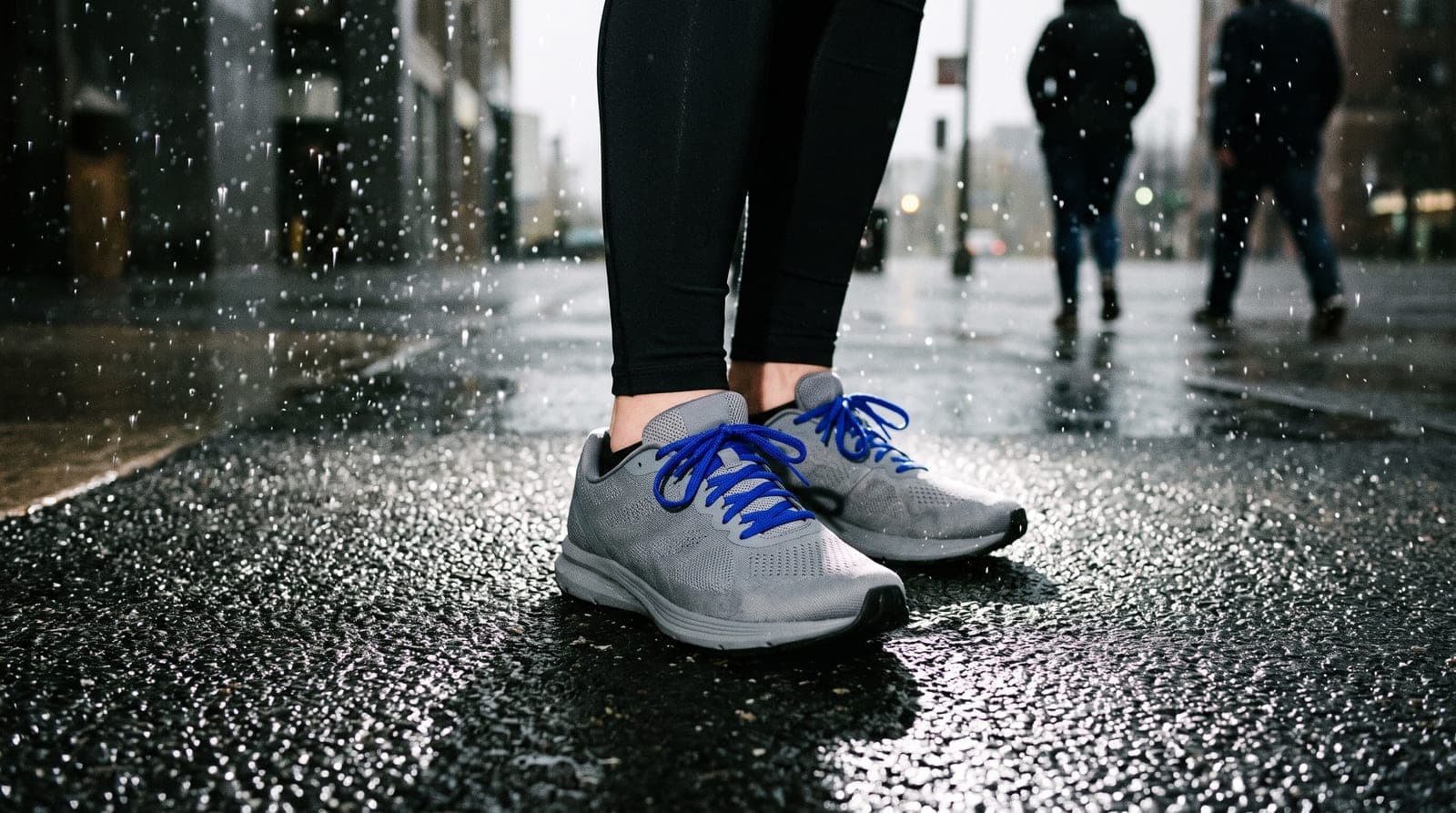 Chaussures de course grises aux lacets bleus sur l'asphalte mouillé, jambes en collant noir, passants avec parapluie au fond