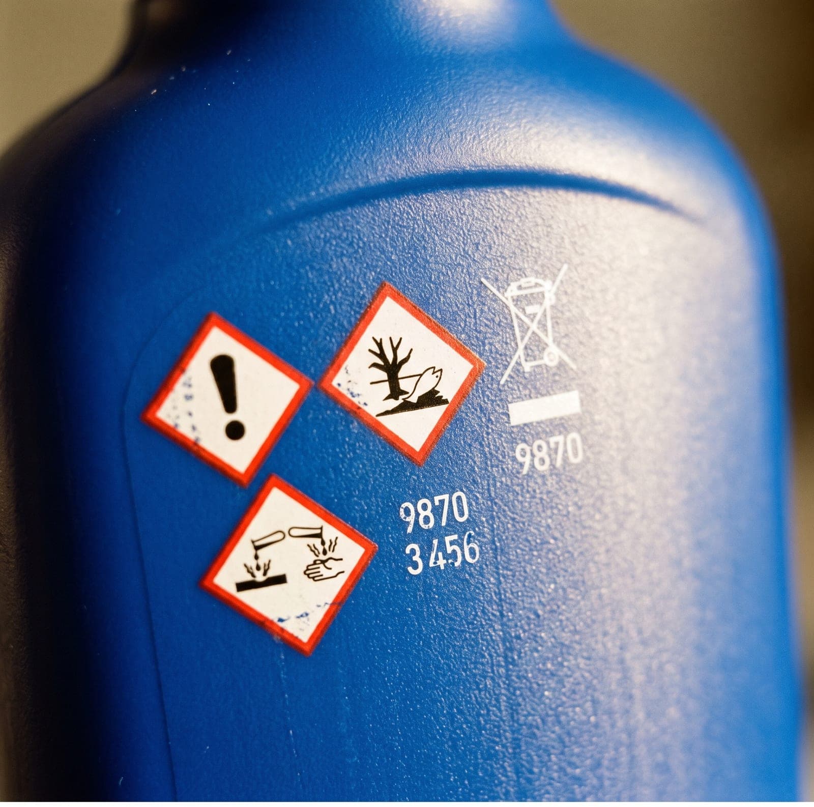 Close-up of the back of a blue plastic bottle, three red-diamond hazard pictograms and a crossed-out bin