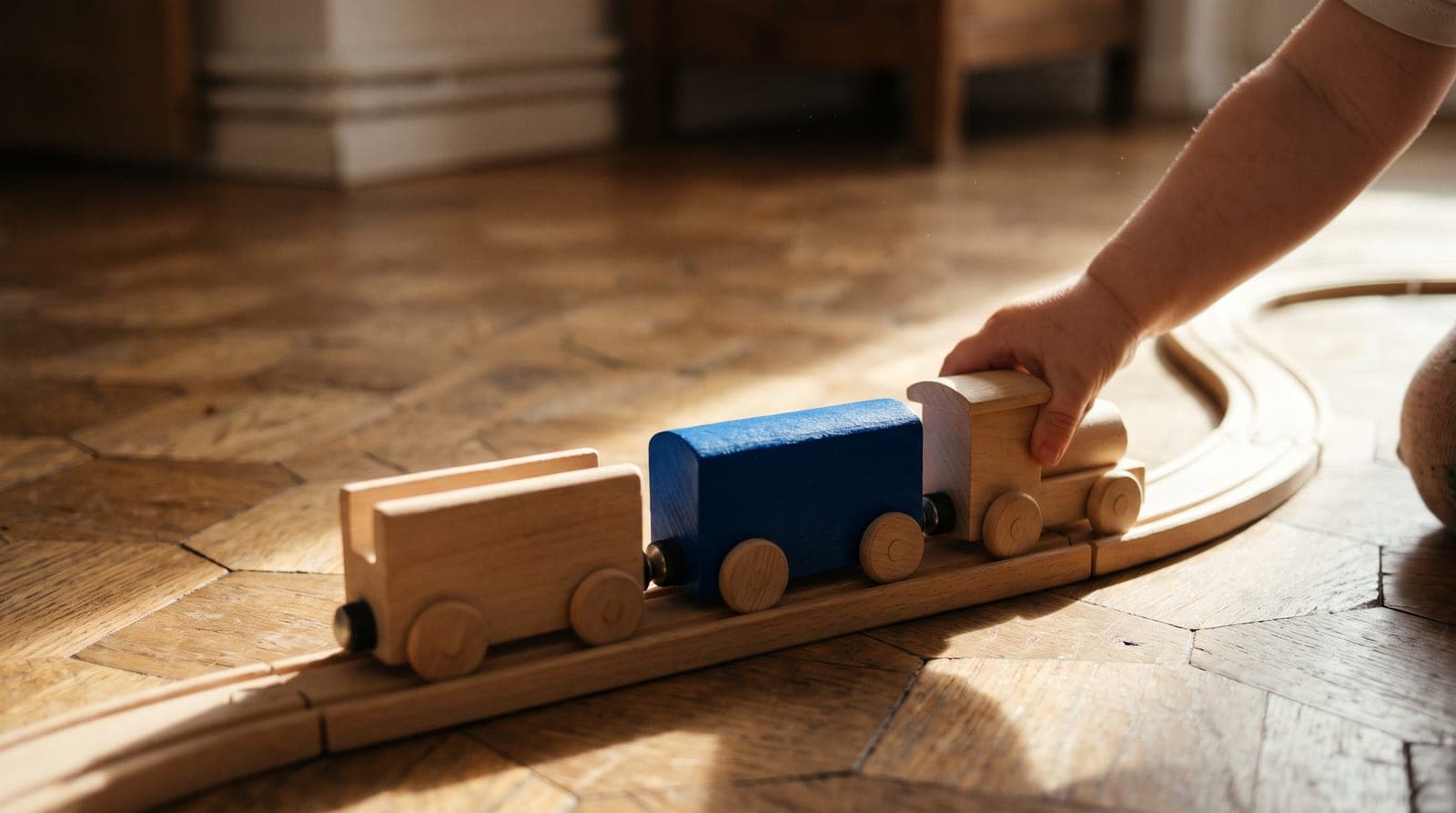 Petit train en bois sur ses rails sur un vieux parquet, un wagon bleu, une main d'enfant pousse la locomotive